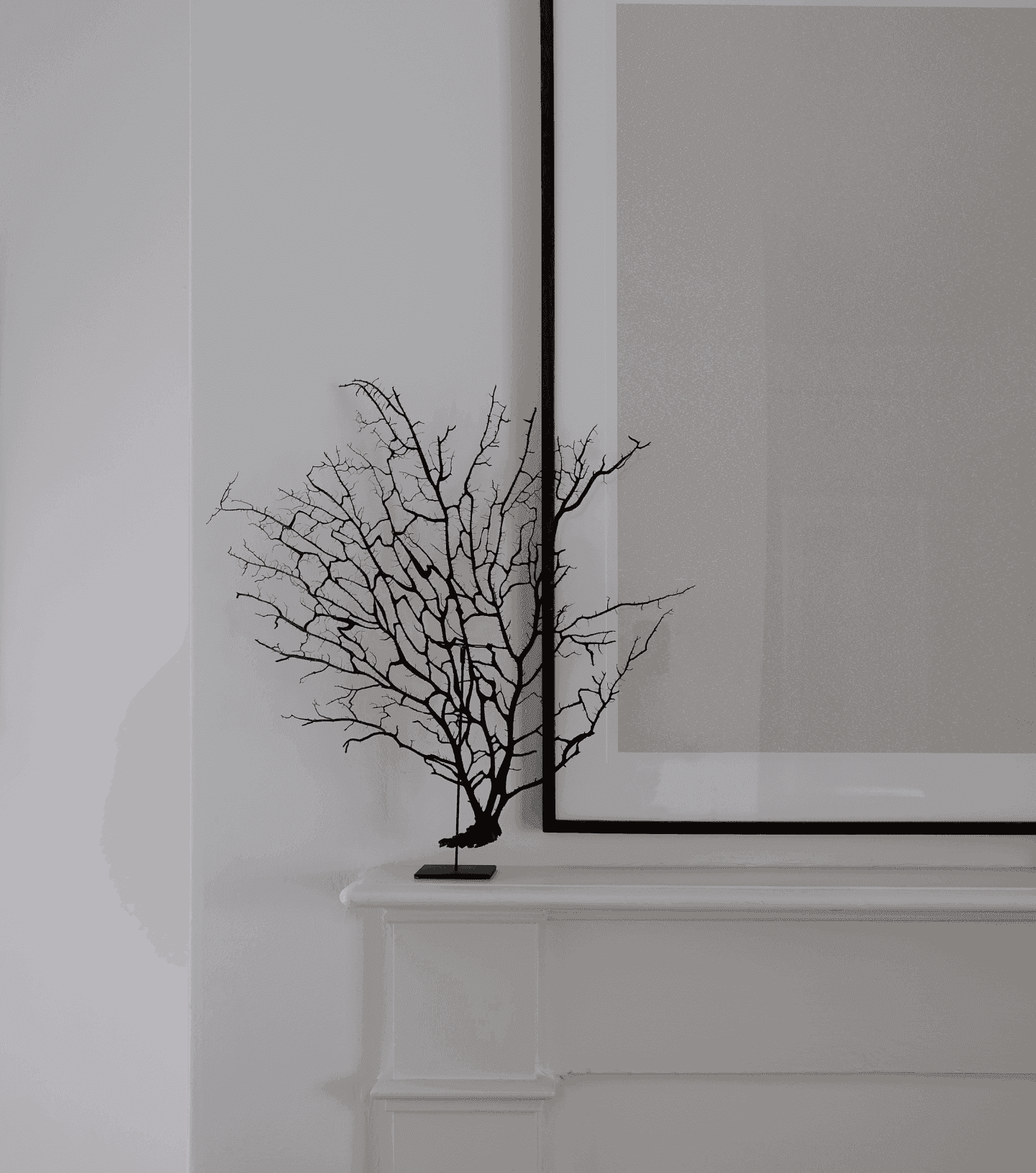 Black sculpture of a tree, on a mantle, in contrast to a white wall.
