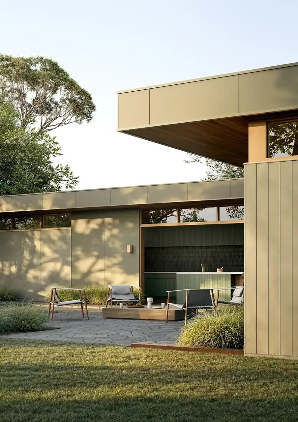 Outdoor sitting pace, with eucalyptus green panels and trim on a modern designer house. Later afternoon sunlight casts lines across the grass and pavers